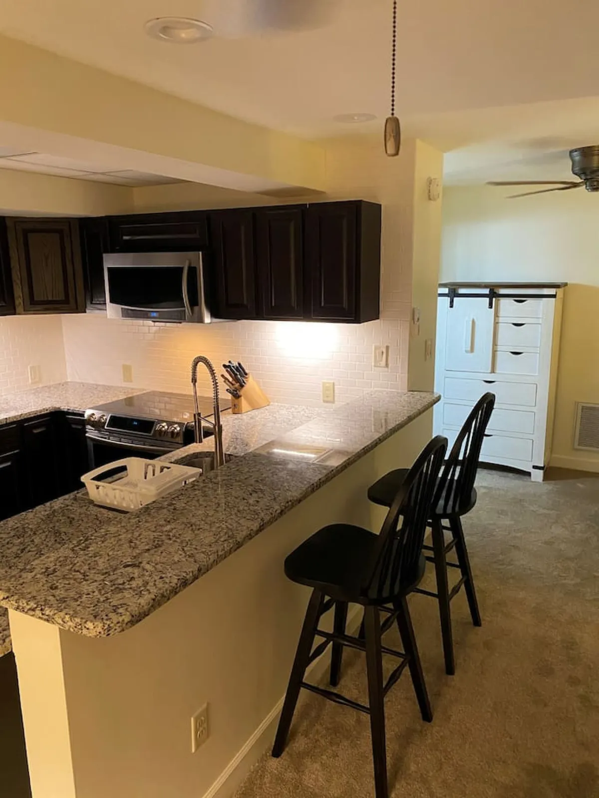 A cozy kitchen scene featuring a gleaming granite countertop, comfortable bar stools, and modern kitchen appliances. The space is bathed in warm light, inviting guests to gather for coffee or share a meal. The open setup encourages socializing and relaxation, with everything needed for cooking or entertaining within easy reach.