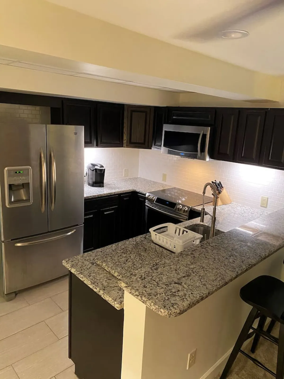 This image showcases a cozy and functional kitchen with a stainless steel refrigerator, granite countertop, modern stove, and a kitchen sink. The setup feels inviting and is suitable for both cooking and casual dining, with ample space for meal preparation and family gatherings.