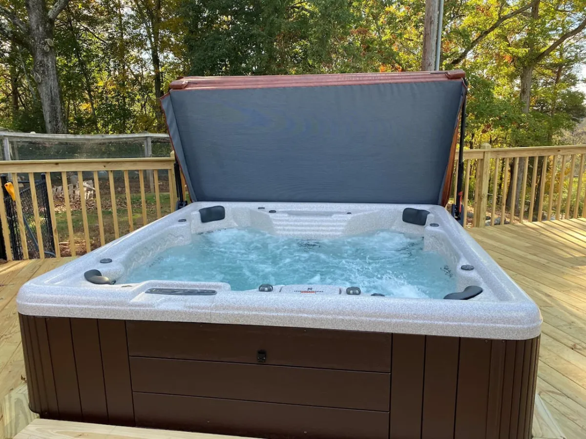 Set in a serene outdoor space, this image highlights a hot tub on a wooden deck enveloped by natural greenery. The scene exudes tranquility, with soft natural light suggesting either sunset or early evening, creating an ideal mood for unwinding after a day of exploration.