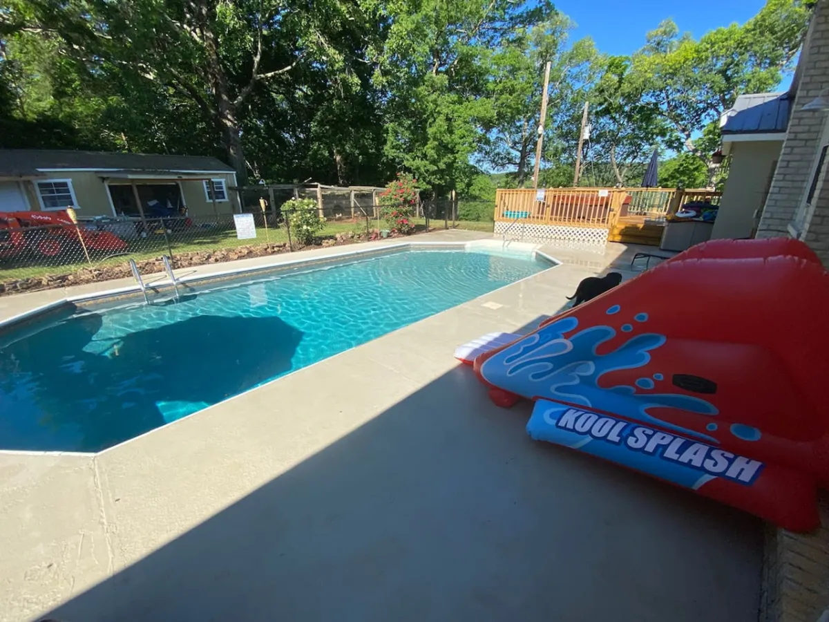 This exterior image centers on a vibrant swimming pool, flanked by a bright red inflatable slide and surrounded by lush greenery and a spacious deck area. The pool's welcoming blue water and the lively atmosphere suggest a setting perfect for both relaxation and fun-filled activities, with ample space for lounging and family gatherings.